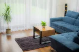 Aranżacja salonu z ciemnym dywanem, niebieską sofą i drewnianym stolikiem