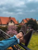 Brązowe ocieplane kapcie na stopach opartych o balustradę